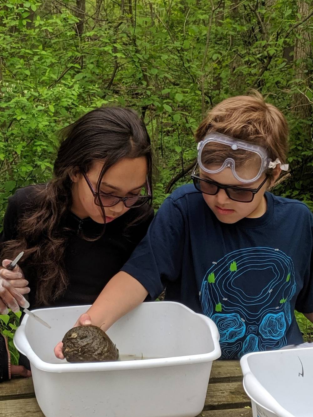 Two students look at rock in a bucket of water